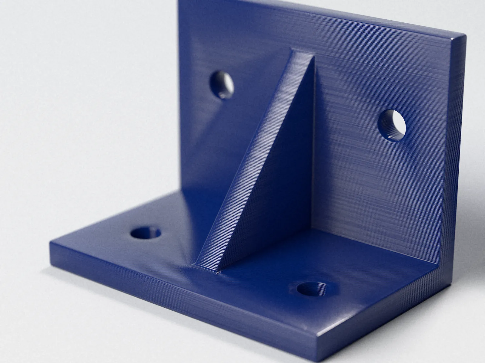 Soporte en L impreso en PETG azul, con nervio de refuerzo y agujeros para fijación