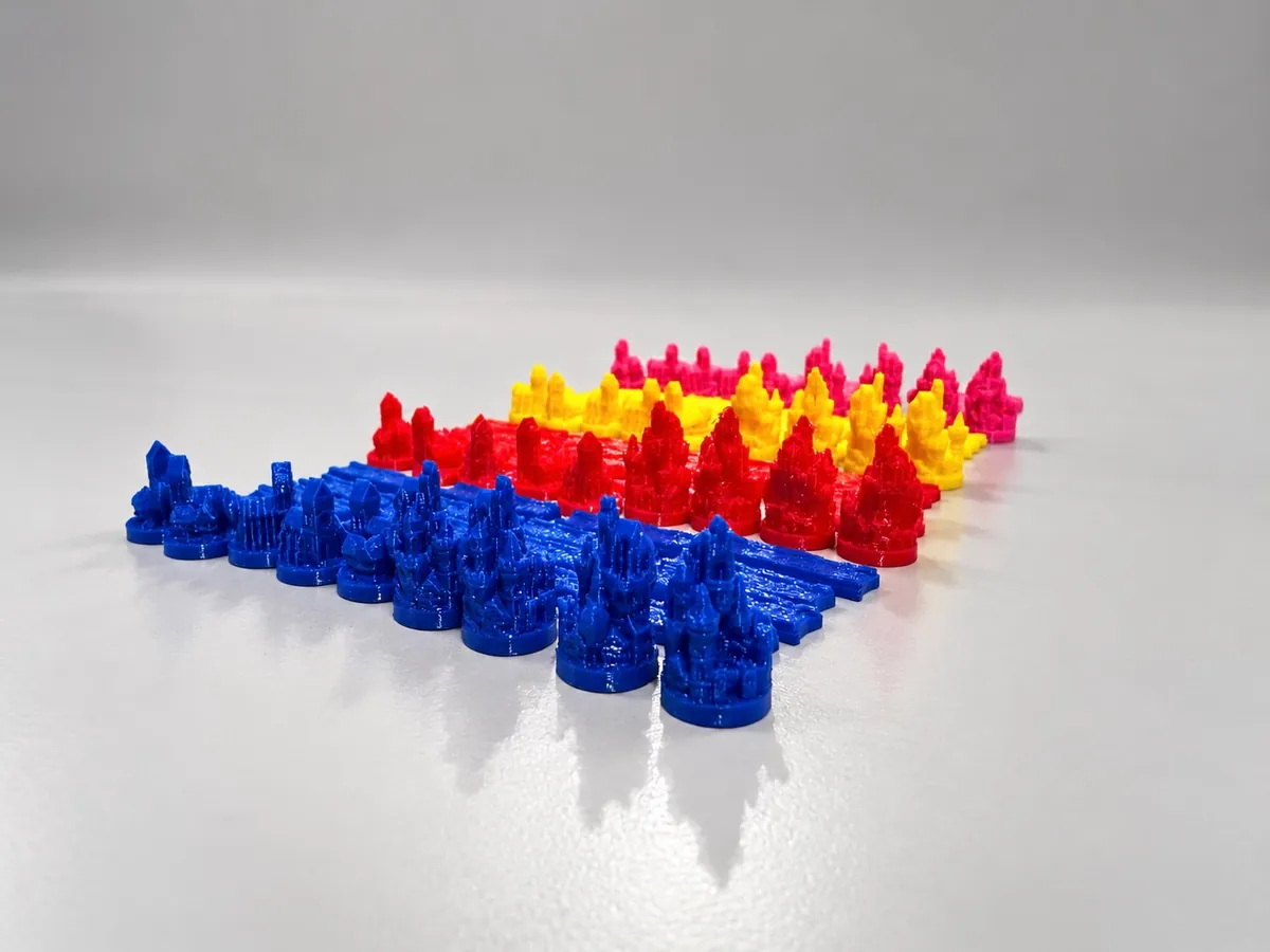 Fichas de juego impresas en 3D en azul, rojo, amarillo y rosa, con forma de castillos y figuras