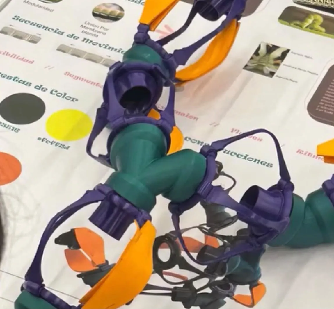 Prototipo articulado impreso en 3D en violeta, verde y naranja, apoyado sobre una lámina de presentación