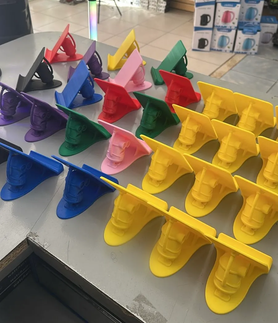 Decenas de soportes para celular impresos en 3D en amarillo, azul, rojo, verde, violeta y rosa, sobre un mostrador